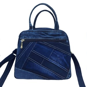 May include: A blue denim handbag featuring a patchwork design with various shades of blue fabric. The bag includes two top handles, a long shoulder strap, and a horizontal zippered pocket on the front with a metallic zipper pull.