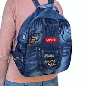 May include: Blue denim backpack with multiple pockets, zippers, and adjustable straps. Features a red "Levi's" logo and "Fashion Denim Boys Jeans" text. The backpack has a classic jeans pocket design.