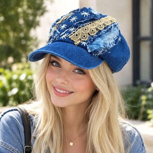 May include: A blue denim newsboy cap featuring distressed fabric patches, white embroidered star-like patterns, and a decorative strip of beige lace trim. The hat has a structured brim and a multi-layered, textured design with frayed edges.