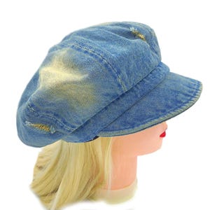 May include: A blue denim newsboy cap with a distressed, worn look. The cap has a rounded crown, a short brim, and visible stitching. The denim has faded patches and small tears, giving it a vintage appearance. The hat is displayed on a mannequin head.