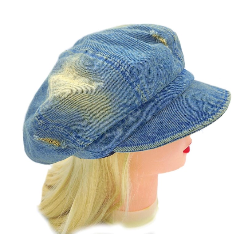 May include: A blue denim newsboy cap with a distressed, worn look. The cap has a rounded crown, a short brim, and visible stitching. The denim has faded patches and small tears, giving it a vintage appearance. The hat is displayed on a mannequin head.