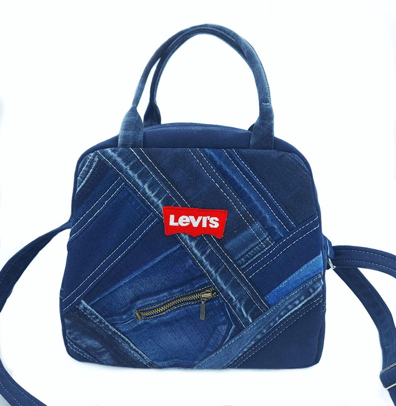 May include: A blue denim handbag featuring a patchwork design of various denim shades arranged in diagonal strips. The bag includes two top handles, a shoulder strap, a brass-colored zipper pocket, and a red Levi's brand label on the front.