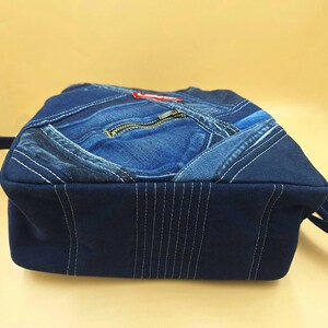 May include: A dark blue denim crossbody bag constructed from repurposed jeans fabric. The bag features a patchwork design with visible seams, a front zipper pocket, and a red Levi's brand tag. It includes a matching dark blue fabric shoulder strap.
