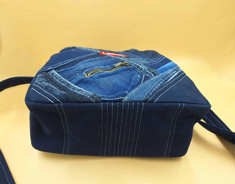 May include: A dark blue denim crossbody bag constructed from repurposed jeans fabric. The bag features a patchwork design with visible seams, a front zipper pocket, and a red Levi's brand tag. It includes a matching dark blue fabric shoulder strap.