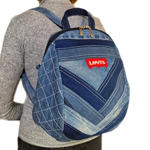 Puede incluir: Una mochila de mezclilla confeccionada con varios tonos de tela de jean azul en un patrón de chevrón. La bolsa cuenta con un parche rojo de la marca Levi's, un asa superior, dos correas para los hombros y un panel lateral con diseño acolchado.
