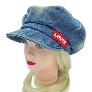 May include: A blue denim cap with a short brim. The cap has a distressed look with a red Levi's logo patch on the side. The cap is displayed on a mannequin head with blonde hair and red lipstick.