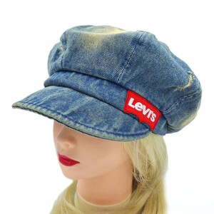 May include: A blue denim newsboy cap with a short brim. The cap features a red Levi's logo patch on the side. The denim has a faded, worn look.