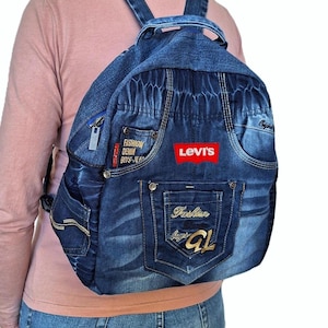 May include: Blue denim backpack with multiple pockets and a zipper closure. Features the Levi's logo in red and text that reads "Fashion Denim Boys-Jeans". The backpack has adjustable straps.