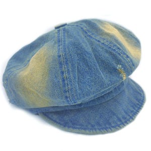 May include: A blue denim newsboy cap with a slightly faded, distressed appearance. The cap features a rounded crown, a short brim, and visible stitching details. The denim has a worn look with lighter patches.