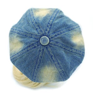 May include: A blue denim newsboy cap with a faded, distressed appearance. The cap features a button on top and a rounded shape. The hat is a fashion accessory.