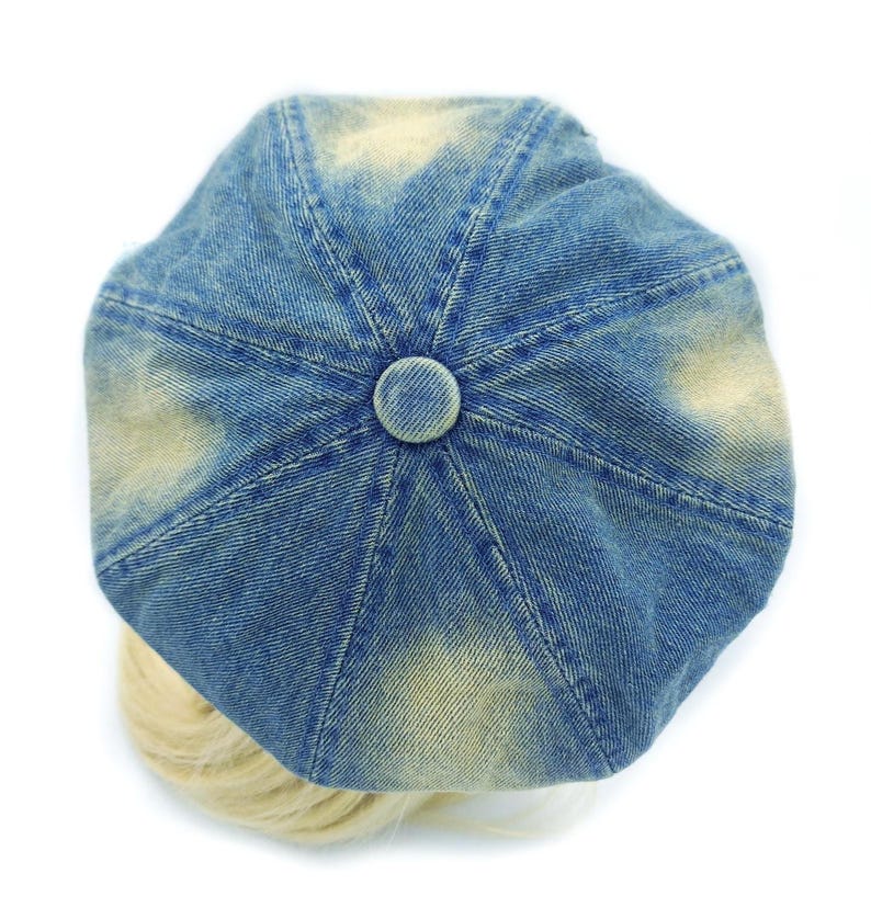 May include: A blue denim newsboy cap with a faded, distressed appearance. The cap features a button on top and a rounded shape. The hat is a fashion accessory.