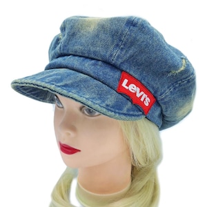 May include: A blue denim cap with a short brim and a red Levi's logo patch. The cap is worn by a mannequin head with blonde hair and red lipstick. The denim has a faded, worn look.
