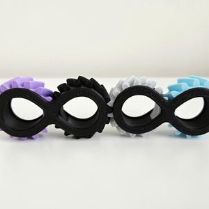 May include: Four infinity-shaped objects in a row, each with a black base and a different colored gear-like accent. Colors include purple, black, gray, and light blue. The objects are on a white surface.