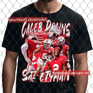 May include: Black t-shirt with a graphic of football players wearing red and white uniforms. The text "Caleb Downs" is written in white with a red outline. The text "Safetyman" is written in white with a red outline. The text "foteini anastoli" is written in white with a red outline.