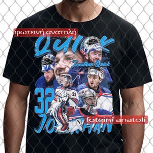 Può includere: T-shirt nero con un collage di un portiere di hockey, con il nome "Jonathan Quick" e il numero "32" in blu. La maglietta include testo in greco.