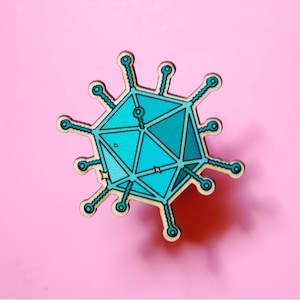 Pode incluir: Um alfinete geométrico em forma de vírus ou bacteriófago, apresentando um corpo central icosaédrico em tons de azul e verde-azulado com braços finos e radiantes que terminam em pequenos círculos. O design tem uma borda de madeira clara.
