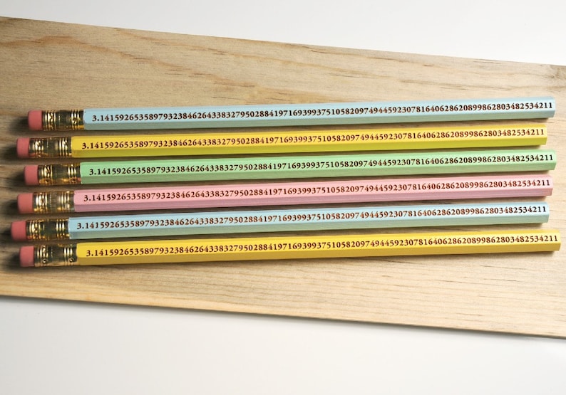 May include: A collection of six pencils in various pastel colors, each with the digits of pi printed along the side. The pencils have pink erasers and gold-colored metal bands. They are arranged on a light-colored wooden surface.