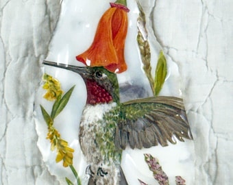 May include: Hand-painted hummingbird pendant on a white, irregular-shaped shell. The hummingbird has green, red, and white feathers, with a long black beak. An orange flower and sprigs of yellow and purple flowers are also painted on the shell.
