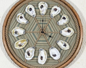 May include: Round wooden clock with a rope border and a striped green and white fabric background. The clock face features oyster shells marking the hours. Black clock hands point to the time.