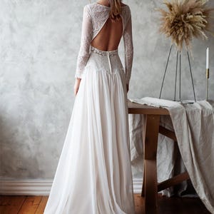May include: A white wedding dress with a flowing skirt and long lace sleeves. The back of the dress features a keyhole design. The dress is made of a soft, lightweight fabric, perfect for a wedding.