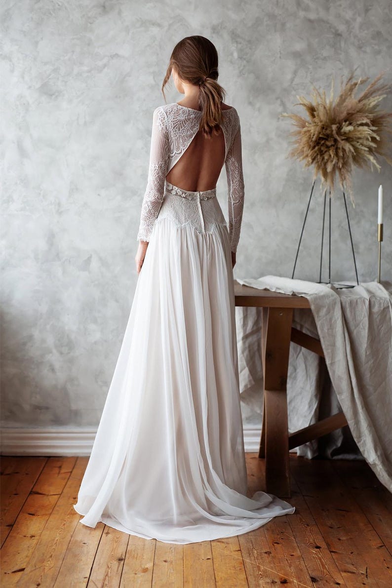 May include: A white wedding dress with a flowing skirt and long lace sleeves. The back of the dress features a keyhole design. The dress is made of a soft, lightweight fabric, perfect for a wedding.