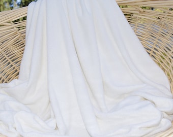 May include: A white plush blanket folded and displayed in a wicker basket.