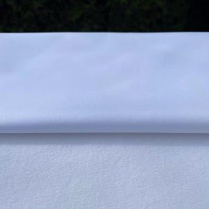 Peut inclure: Un tissu satiné blanc avec une texture lisse et soyeuse. Le tissu est plié en deux, révélant le dessous.