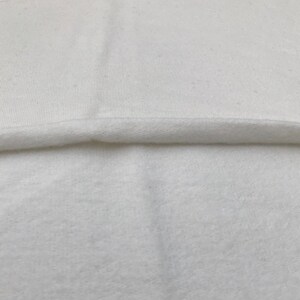 Puede incluir: Primer plano de una tela blanca con una textura suave y peluda. La tela est&aacute; doblada por la mitad, mostrando el lado liso y el lado peludo.