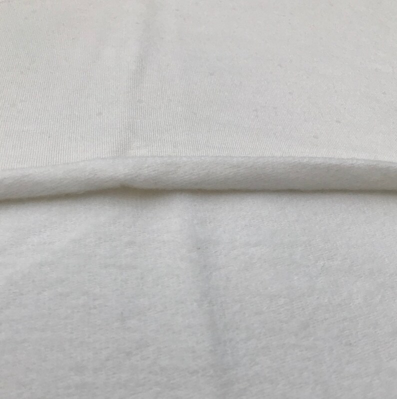 Puede incluir: Primer plano de una tela blanca con una textura suave y peluda. La tela est&aacute; doblada por la mitad, mostrando el lado liso y el lado peludo.
