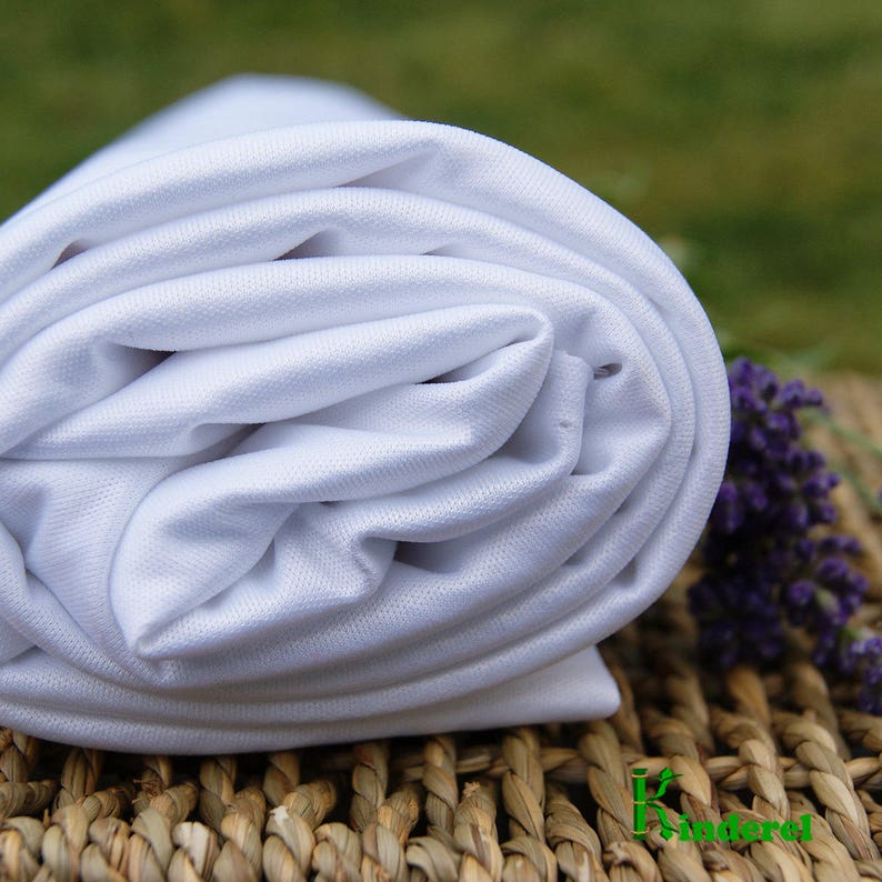 May include: A white, tightly rolled fabric with a smooth texture. The fabric is lying on a woven surface with a light brown color.