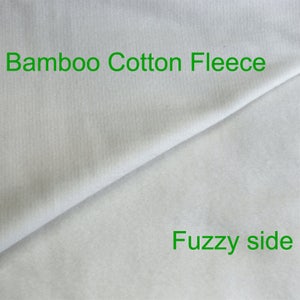 Może przedstawiać: Zbliżenie na białą tkaninę z gładką stroną i puszystą stroną. Tkanina jest oznaczona jako "Bamboo Cotton Fleece" i "Fuzzy side".