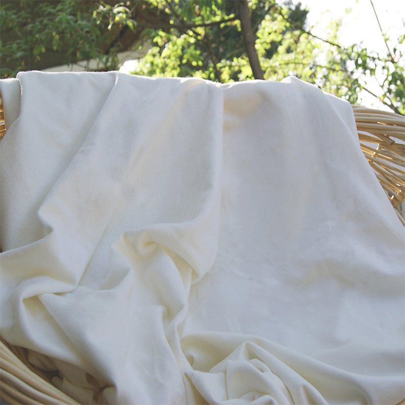 May include: A white cotton fabric draped over a wicker basket. The fabric is soft and smooth, with a natural, unbleached look.
