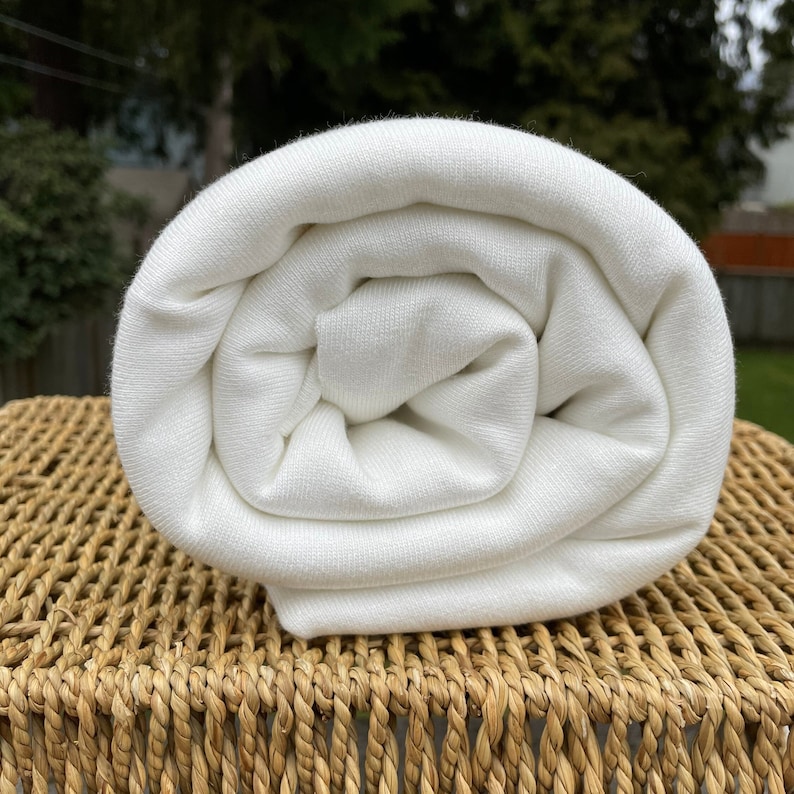 May include: A white, rolled up piece of fabric. The fabric is smooth and has a slight sheen.
