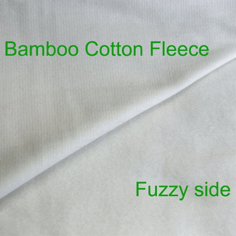 May include: Close-up of a white bamboo cotton fleece fabric. The fabric has a smooth side and a fuzzy side. The text "Bamboo Cotton Fleece" is printed on the smooth side and the text "Fuzzy side" is printed on the fuzzy side.