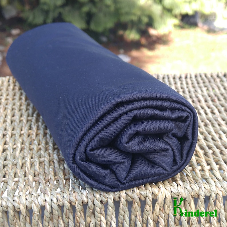 May include: A dark blue fabric rolled up on a woven surface. The fabric is smooth and has a slight sheen.