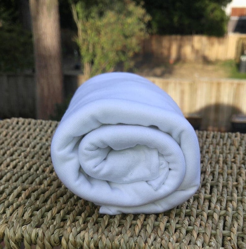 May include: A white fabric rolled up on a woven surface. The fabric is soft and smooth.