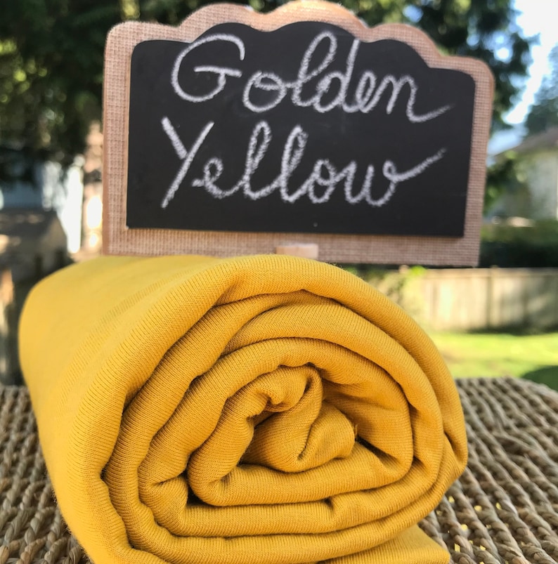May include: A roll of golden yellow fabric. The fabric is soft and stretchy, and it is perfect for sewing projects.