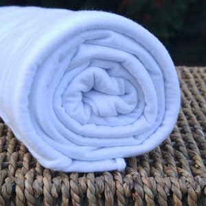 May include: A white, rolled up piece of fabric, possibly a t-shirt or a piece of clothing, sitting on a woven wicker surface.