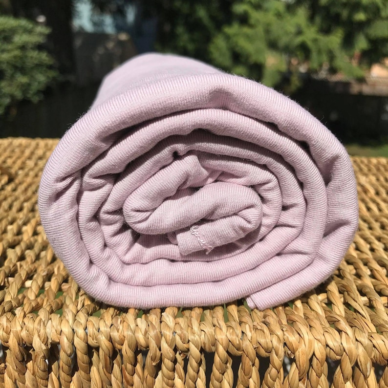 May include: A roll of soft, light purple fabric. The fabric is ribbed and has a smooth texture.