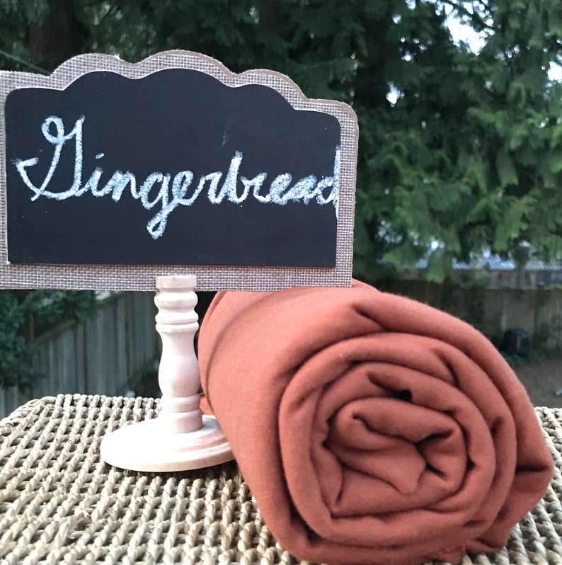 May include: A rolled up rust-colored fabric with a sign that says "Gingerbread" on a wooden stand.