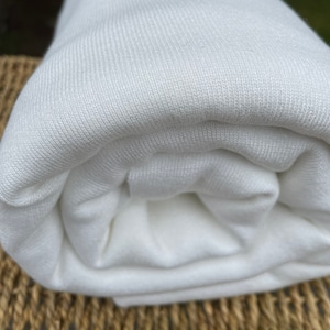May include: A close-up of a white ribbed fabric rolled up. The fabric is soft and smooth.