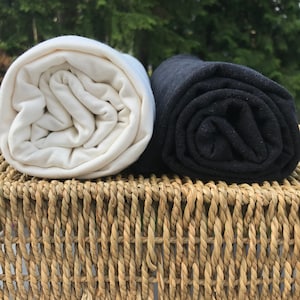 May include: Two rolled up pieces of fabric, one white and one black, sitting on a woven basket.