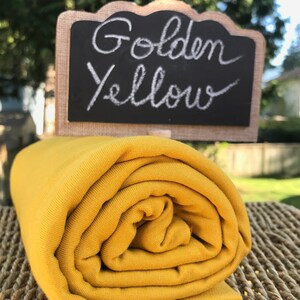 May include: A roll of golden yellow fabric. The fabric is soft and stretchy, and it is perfect for sewing projects.