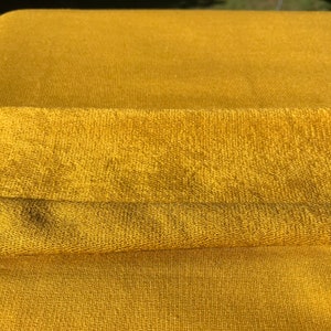 May include: A close-up of a folded piece of mustard yellow fabric with a textured surface.