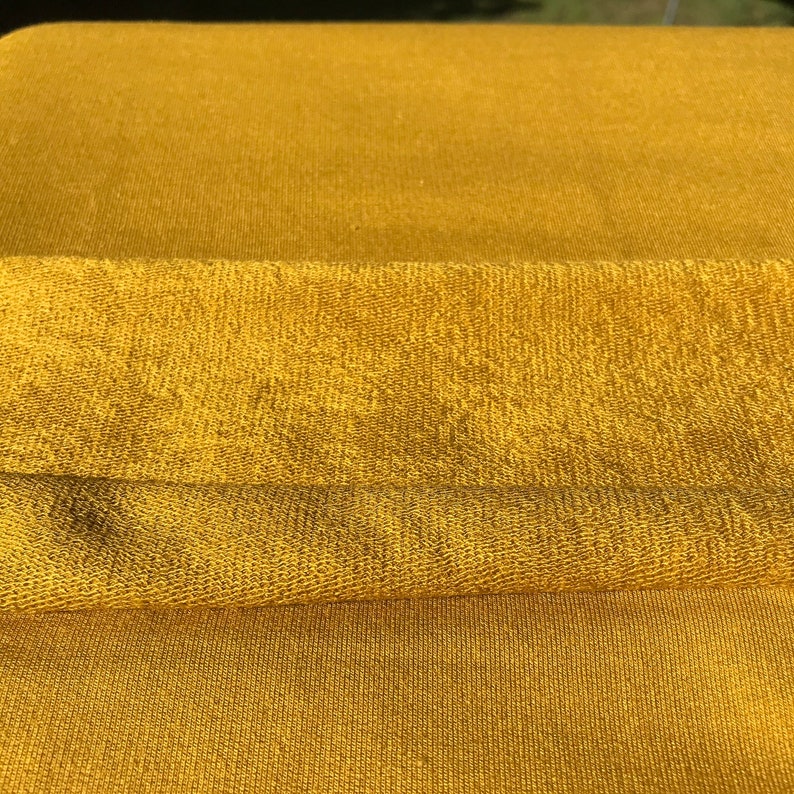 May include: A close-up of a folded piece of mustard yellow fabric with a textured surface.