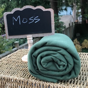 May include: A roll of dark green fabric labeled "Moss" on a woven wicker surface.