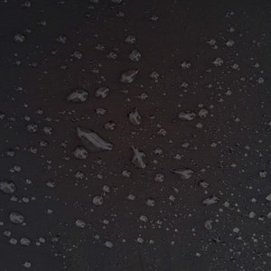 May include: A close-up of a black surface with many small water droplets scattered across it.