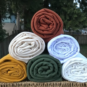 May include: Five rolls of fabric in different colors: rust, cream, white, forest green, and mustard yellow. The fabric is rolled up and stacked on top of each other.