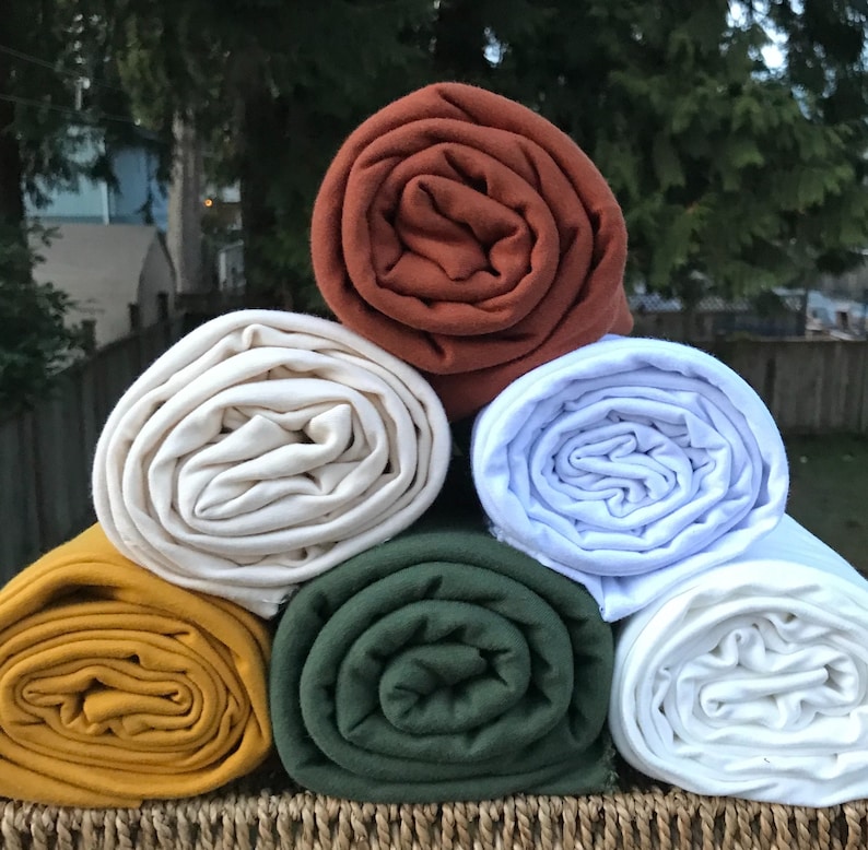May include: Five rolls of fabric in different colors: rust, cream, white, forest green, and mustard yellow. The fabric is rolled up and stacked on top of each other.