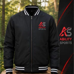 Puede incluir: Una chaqueta bomber negra con cierre de cremallera frontal, cuello acanalado y puños acanalados con rayas blancas. El pecho muestra un logotipo rojo y gris con el texto AS ABILITY SPORTS. El diseño incluye un logotipo a juego en el lateral.